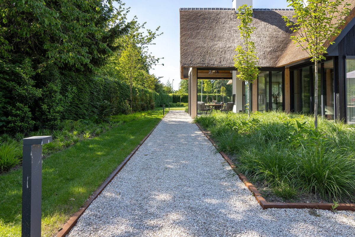Aangelegd tuinpad van split met stalen kantopsluiting langs een border met siergrassen